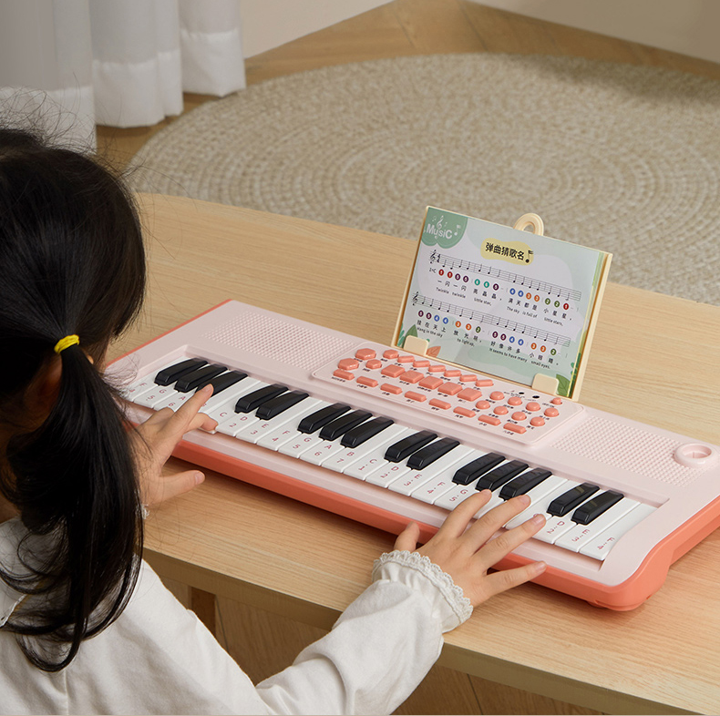 A little girl plays a pink electronic organ at a wooden table