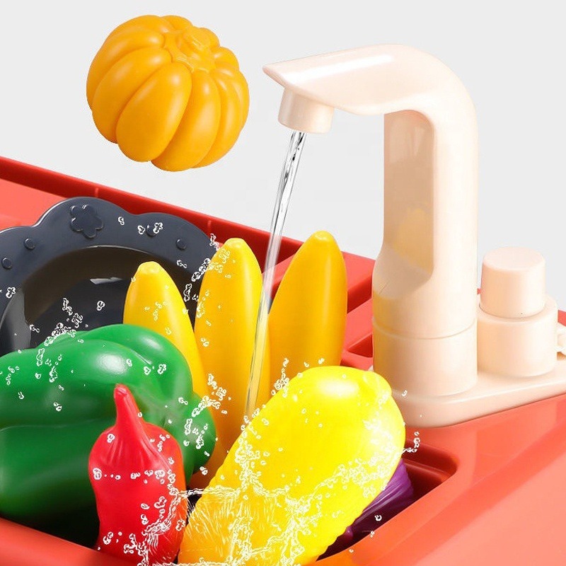The toy faucet is running water to rinse different colored toy fruits and vegetables