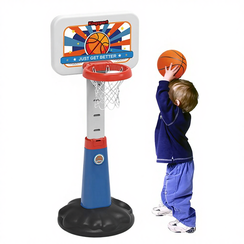 A little boy in a blue outfit stands in front of the basketball stand, holding a basketball and shooting